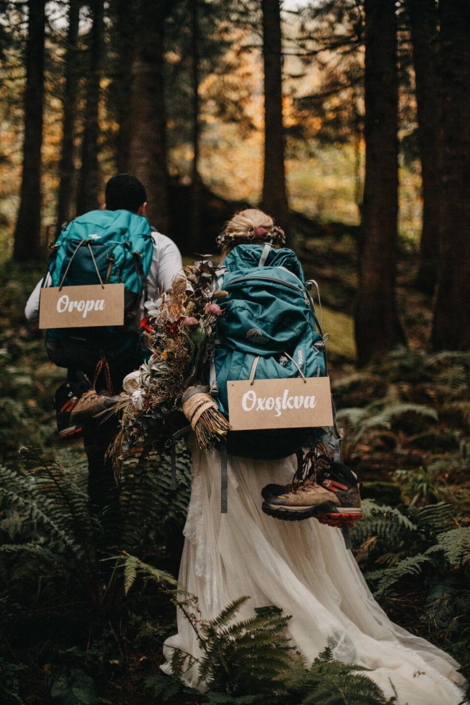 Ein lasisches Pärchen von hinten fotografiert. Sie tragen Hochzeitstracht und dazu Wanderrucksäcke. 