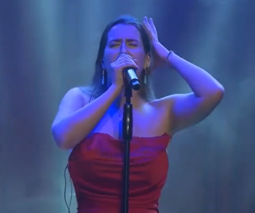 Eine Frau mit langen braunen Haaren, Liana Georgi, steht im roten Kleid auf der Bühne und singt ins Mikrofon.