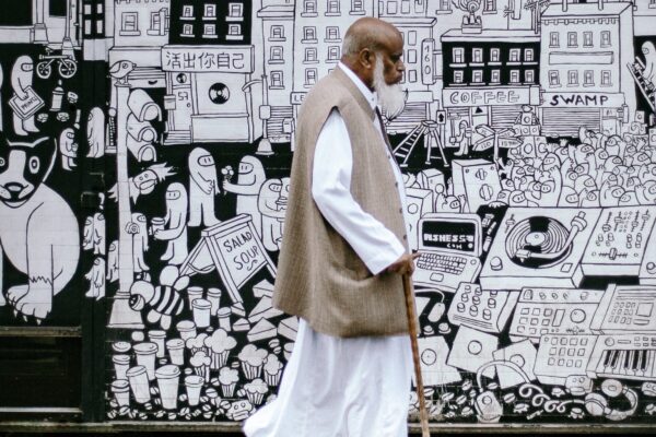 Schwarzer Muslimischer Mann, der von Kulturrassismus betroffen sein kann, läuft an einer künstlerisch gestalteten Wand vorbei.