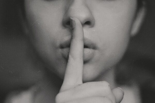 Eine Person, hält sich den Zeigefinger auf die Lippen, um ein Geheimnis zu repräsentieren.
